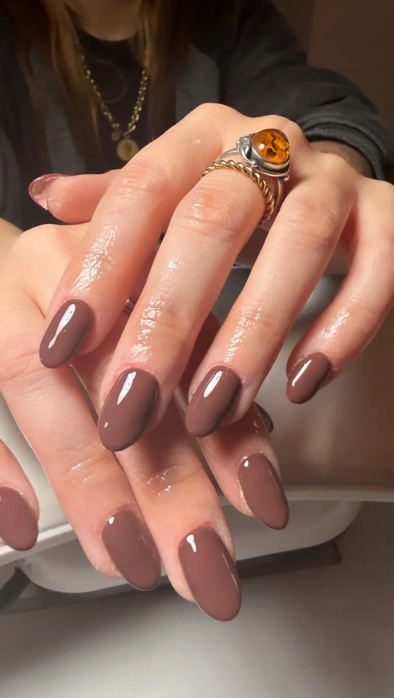 Glossy taupe almond nails worn with an amber ring, by Rosie Mae Beauty